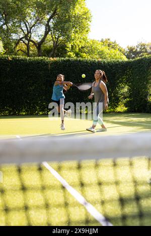 All'aperto, madre e figlia birazziali giocano a tennis insieme su un campo Foto Stock