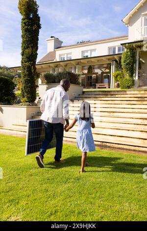 All'aperto, padre e figlia diversi camminano mano nella mano con il pannello solare Foto Stock