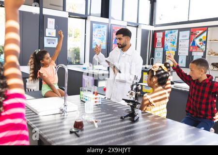 Un giovane insegnante asiatico di sesso maschile insegna a un gruppo eterogeneo di bambini desiderosi in una classe di scienze a scuola Foto Stock