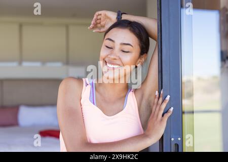 A casa, una giovane donna birazziale che indossa una canotta rosa, appoggiata su un telaio della porta Foto Stock