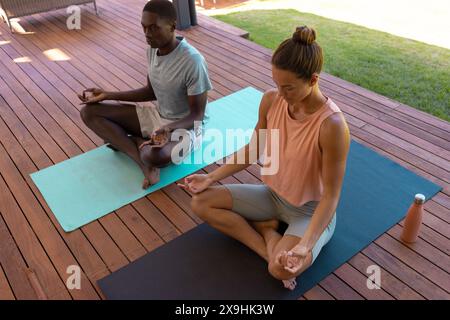 Una coppia giovane e variegata che medita all'aperto su stuoie per yoga Foto Stock