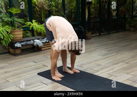 Lo studio Glass House cattura l'istruttore di yoga maschile caucasico che si piega sul tappeto Foto Stock