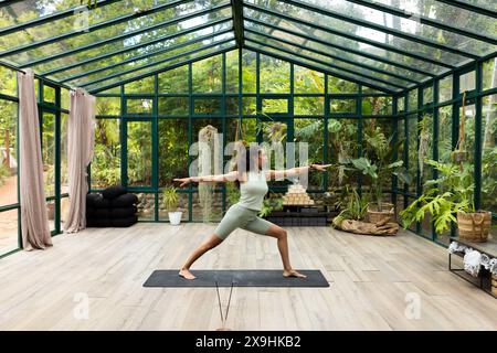 Presso lo studio Glass House, istruttrice di yoga birazziale femminile in verde chiaro Foto Stock