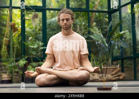 Al Glass House Studio, istruttore di yoga maschile caucasico che meditava con una camicia di pesca Foto Stock