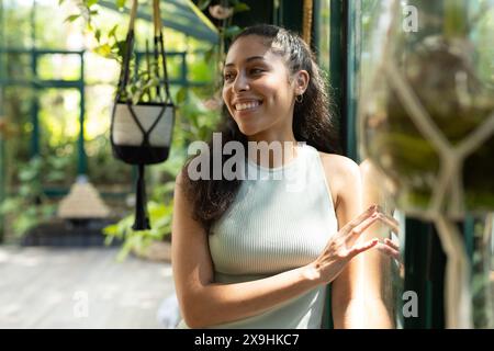 La donna birazziale sorride nella lussureggiante serra del Glass House Studio mentre pratica yoga Foto Stock