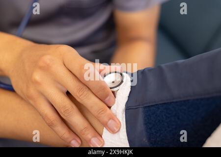 A casa, giovane infermiera birazziale maschile che controlla la BP della paziente anziana. Sono in uno studio medico con sfondo bianco, focalizzato sulla cura del paziente Foto Stock