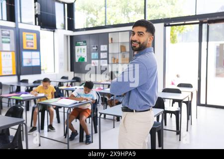 A scuola, l'insegnante maschile asiatico sorride in classe, gli studenti si concentrano sul lavoro Foto Stock