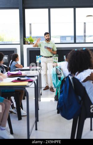 A scuola, un insegnante maschile asiatico sta spiegando agli studenti birazziali Foto Stock