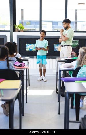 A scuola, la giovane ragazza birazziale sta presentando, con un insegnante asiatico maschile che guarda Foto Stock