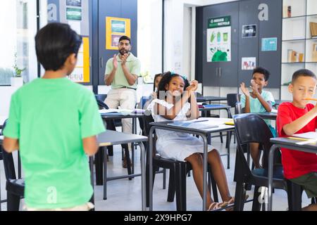 A scuola, un insegnante maschio asiatico batte le mani mentre diversi studenti alzano le mani Foto Stock