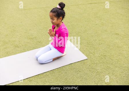 A scuola, la giovane ragazza birazziale che indossa il rosa pratica yoga all'aperto Foto Stock