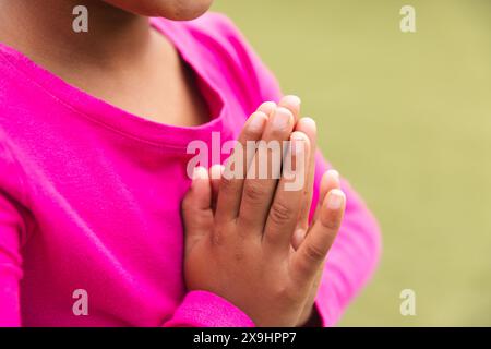 A scuola, una giovane ragazza birazziale con un tetto rosa brillante sta pregando all'aperto e facendo yoga Foto Stock