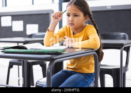 A scuola, giovane ragazza birazziale seduta ad una scrivania in classe, che sembra premurosa Foto Stock