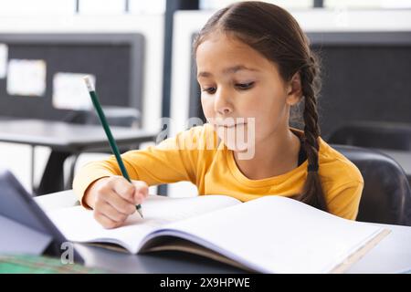 A scuola, giovane ragazza birazziale con capelli intrecciati che si concentra sulla scrittura in classe Foto Stock