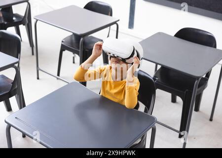 A scuola, in classe, studentessa birazziale che indossa un visore per la realtà virtuale Foto Stock