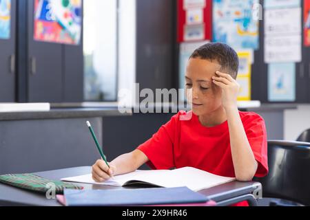 Il ragazzo birazziale si concentra sul suo lavoro scolastico in una classe a scuola Foto Stock