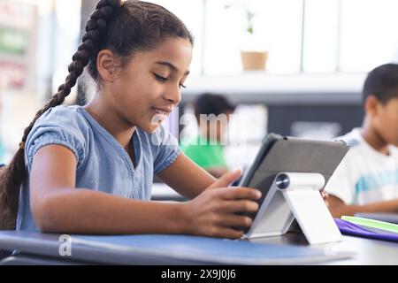 A scuola, giovane studentessa birazziale che usa un tablet in classe Foto Stock