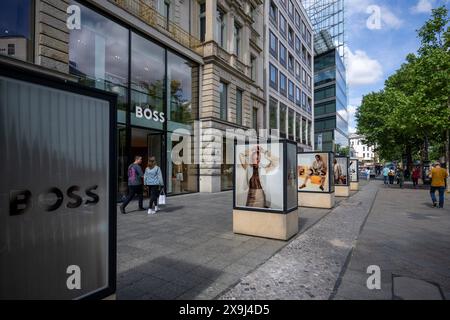 31 maggio 2024, Berlino: Passanti a piedi lungo Kurfürstendamm passando davanti a un negozio di marca Boss. Kurfürstendamm, conosciuta anche come Ku'damm, è una delle più grandi vie dello shopping di Berlino ed è considerata un punto di riferimento della capitale. Foto: Monika Skolimowska/dpa Foto Stock