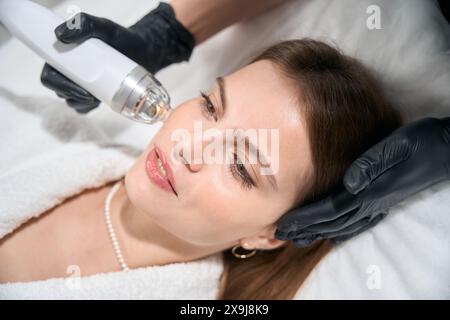 Vista dall'alto del cosmetologo che esegue il sollevamento rf microneedle della pelle del viso della donna Foto Stock