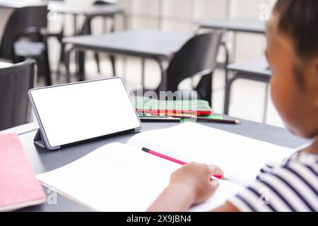 A scuola, una giovane ragazza birazziale sta scrivendo in un quaderno in classe, con spazio per le copie Foto Stock