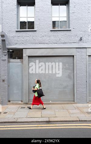 Vista su Gv di una donna solitaria che cammina accanto a un negozio chiuso a Shoreditch East London, Regno Unito Foto Stock