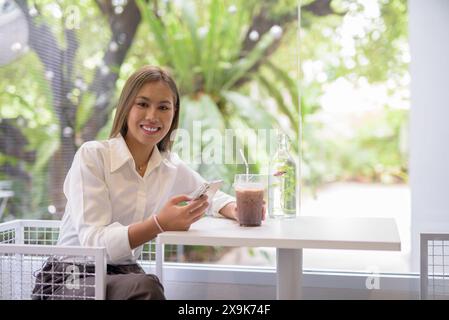 Donna d'affari professionale che lavora sul suo smartphone in un bar luminoso e moderno con caffè e vegetazione Foto Stock