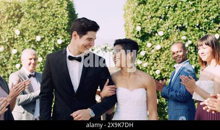 Coppia, felice e matrimonio con applausi, celebrazione e sorriso per matrimonio, impegno e amore. Sposa, sposo e famiglia insieme alla folla Foto Stock