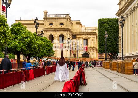 Settimana Santa di Siviglia (Semana Santa), un uomo in tradizionale abito religioso bianco e cappa appuntita (capirote) che cammina lungo il viale della Costituzione in Spagna. Foto Stock