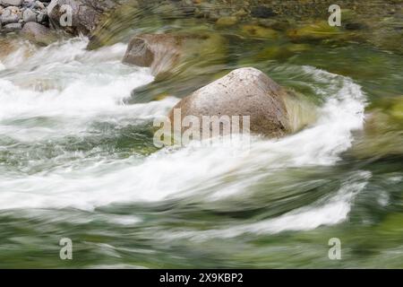Il flusso d'acqua dolce pulita scorre al rallentatore con linee setose intorno alla roccia del fiume in primavera Foto Stock