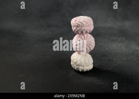 Morbidi e soffici marshmallow bianchi e rosa contrastano splendidamente con uno sfondo nero. Una composizione visivamente accattivante, perfetta per la Foto Stock