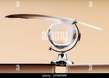 Globo di vetro con piuma d'uccello bilanciata sulla pila di libri, fragile equilibrio del concetto di ecosistema terrestre Foto Stock