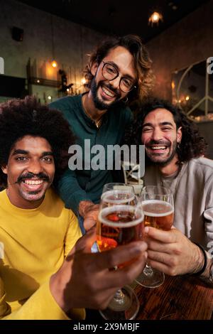 Ritratto di un gruppo multirazziale di tre uomini amici che guardano la macchina fotografica mentre brindano con le birre. Foto Stock
