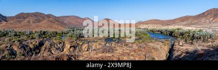 Panorama, fiume Kunene con vegetazione verde nel paesaggio secco delle montagne rosse, cascata e baobab africano (Adansonia digitata), alla luce della sera Foto Stock