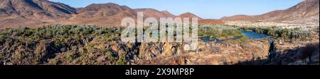 Panorama, fiume Kunene con vegetazione verde nel paesaggio secco delle montagne rosse, cascata e baobab africano (Adansonia digitata), alla luce della sera Foto Stock
