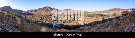 Panorama, fiume Kunene con vegetazione verde nel paesaggio secco delle montagne rosse, cascata e baobab africano (Adansonia digitata), alla luce della sera Foto Stock