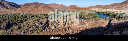 Panorama, fiume Kunene con vegetazione verde nel paesaggio secco delle montagne rosse, cascata e baobab africano (Adansonia digitata), alla luce della sera Foto Stock