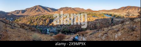 Panorama, fiume Kunene con vegetazione verde nel paesaggio secco delle montagne rosse, cascata e baobab africano (Adansonia digitata), alla luce della sera Foto Stock