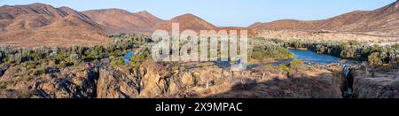 Panorama, fiume Kunene con vegetazione verde nel paesaggio secco delle montagne rosse, cascata e baobab africano (Adansonia digitata), alla luce della sera Foto Stock
