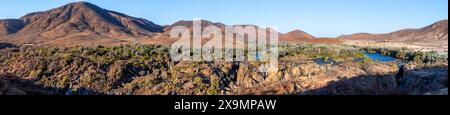 Panorama, fiume Kunene con vegetazione verde nel paesaggio secco delle montagne rosse, cascata e baobab africano (Adansonia digitata), alla luce della sera Foto Stock