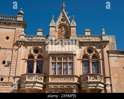 Magnifica facciata con finestre e balconi ornati e un magnifico stemma sotto un cielo blu luminoso, la città di mdina sull'isola di Foto Stock