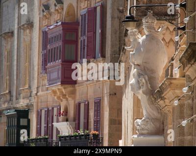 Una facciata dell'edificio con persiane colorate, balconi e una statua, la città di mdina sull'isola di malta con case storiche colorate Foto Stock