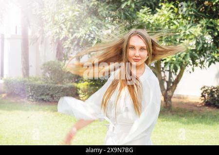 Una ragazza felice con un vestito bianco gira nel cortile Foto Stock