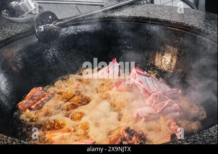 Cucinare carne di agnello in calderone bollente per il tradizionale pilaf uzbeko orientale nella cucina di un ristorante in Uzbekistan Foto Stock