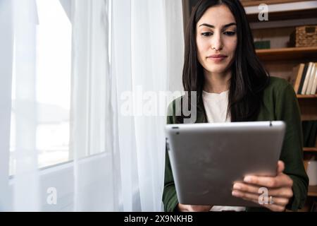 Donna attraente che lavora su un tablet digitale in un ufficio domestico. Donna d'affari proprietaria di una piccola azienda lavora online dal suo appartamento. Freelance indipendente Foto Stock