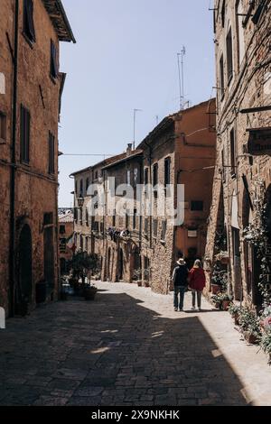 Due turisti che ammirano la splendida vista di una splendida strada stretta nella storica città medievale di Volterra in Toscana, in una giornata di sole. Foto Stock