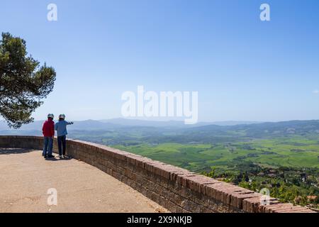 Due turisti che indossano i caschi in un tour in Vespa ammirando il panorama dal classico punto panoramico nella storica città medievale di Volterra in Toscana, Italia Foto Stock