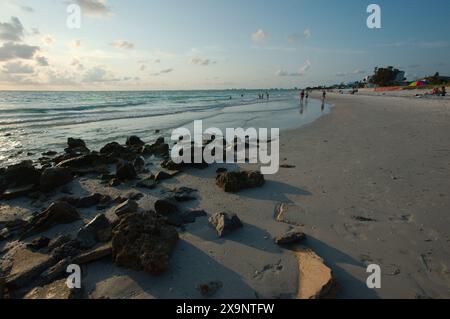 Ampia vista della spiaggia Pass-a-Grille di St. Pete Beach, Florida, guardando a nord. Rocce e molte persone camminano nella sabbia e nell'acqua, vicino al set Foto Stock