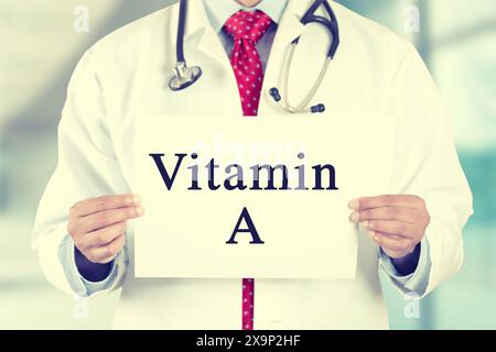 Primo piano mani del medico che tiene in mano il cartello bianco con la vitamina Un messaggio di testo isolato sullo sfondo dell'ufficio della clinica ospedaliera Foto Stock