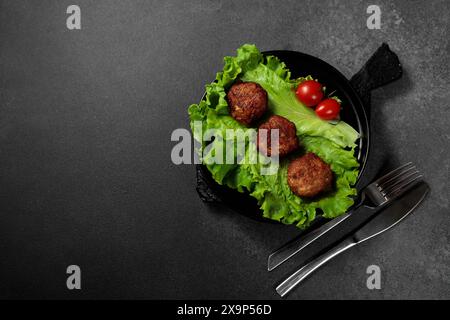 Deliziose cotolette fritte servite su un letto di lattuga croccante, guarnite con fette di pomodoro mature, tutte splendidamente presentate su uno sfondo nero Foto Stock