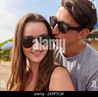 Felice, in coppia o all'aperto per rapporto con occhiali da sole, vacanze al sole o baci. L'uomo, la natura o sussurrando nelle donne l'orecchio per un messaggio segreto Foto Stock